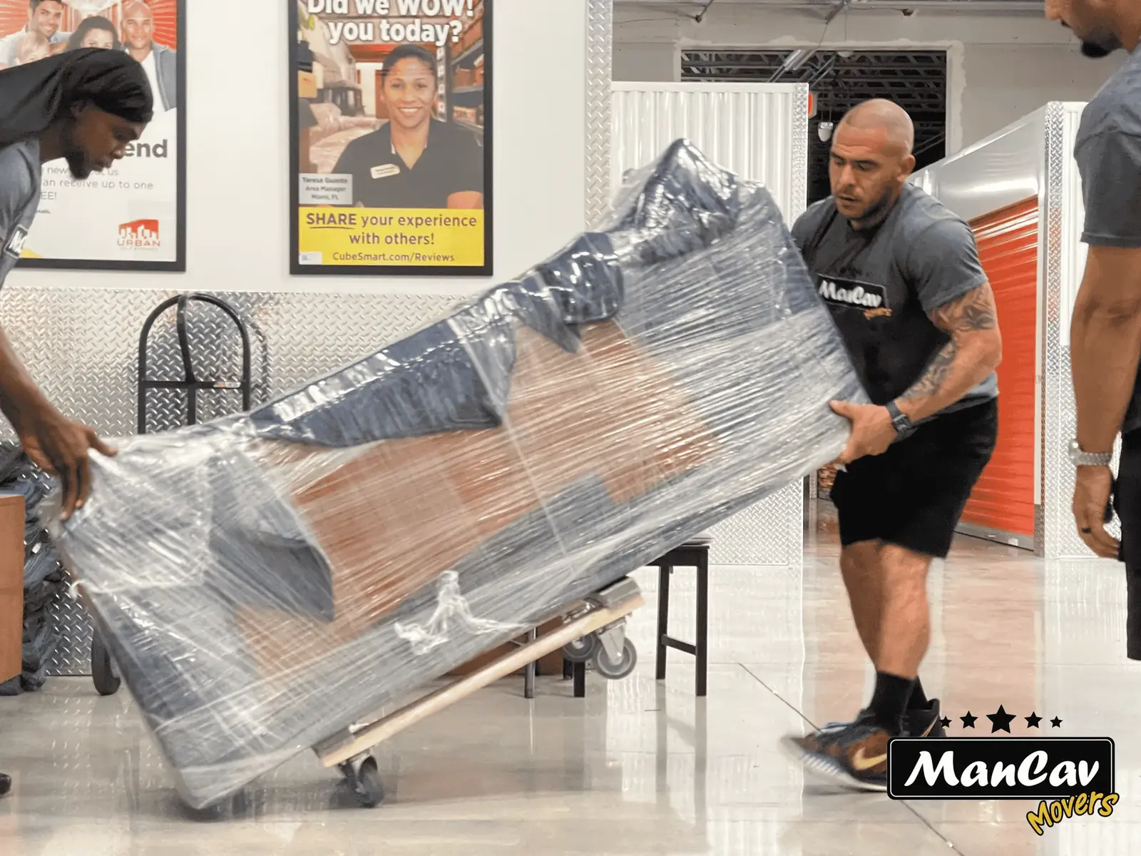ManCav Movers crew moving wrapped furniture on a dolly at a storage facility