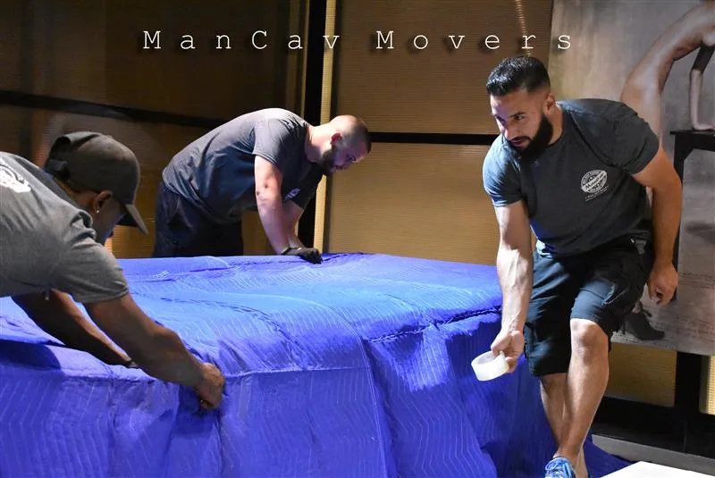 ManCav Movers crew covering furniture with a blue moving blanket