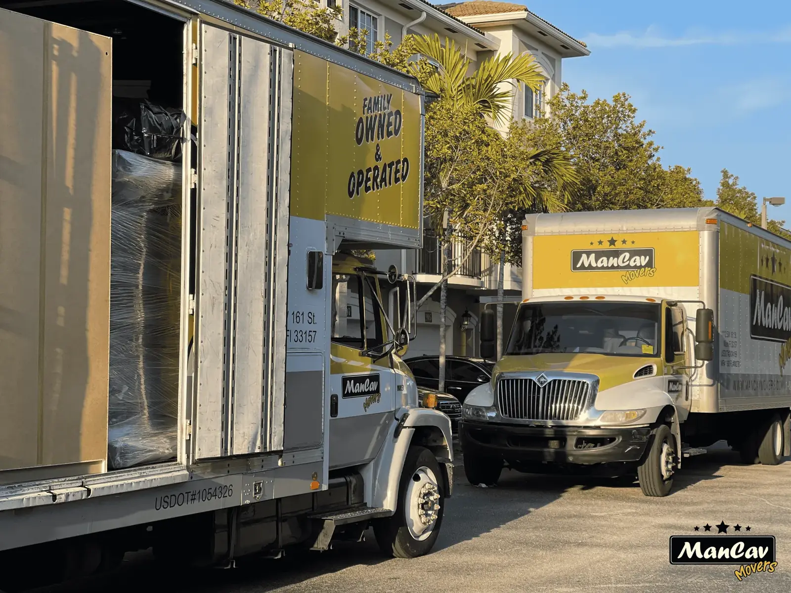Two yellow ManCav Movers box trucks loading furniture, marked family owned and operated