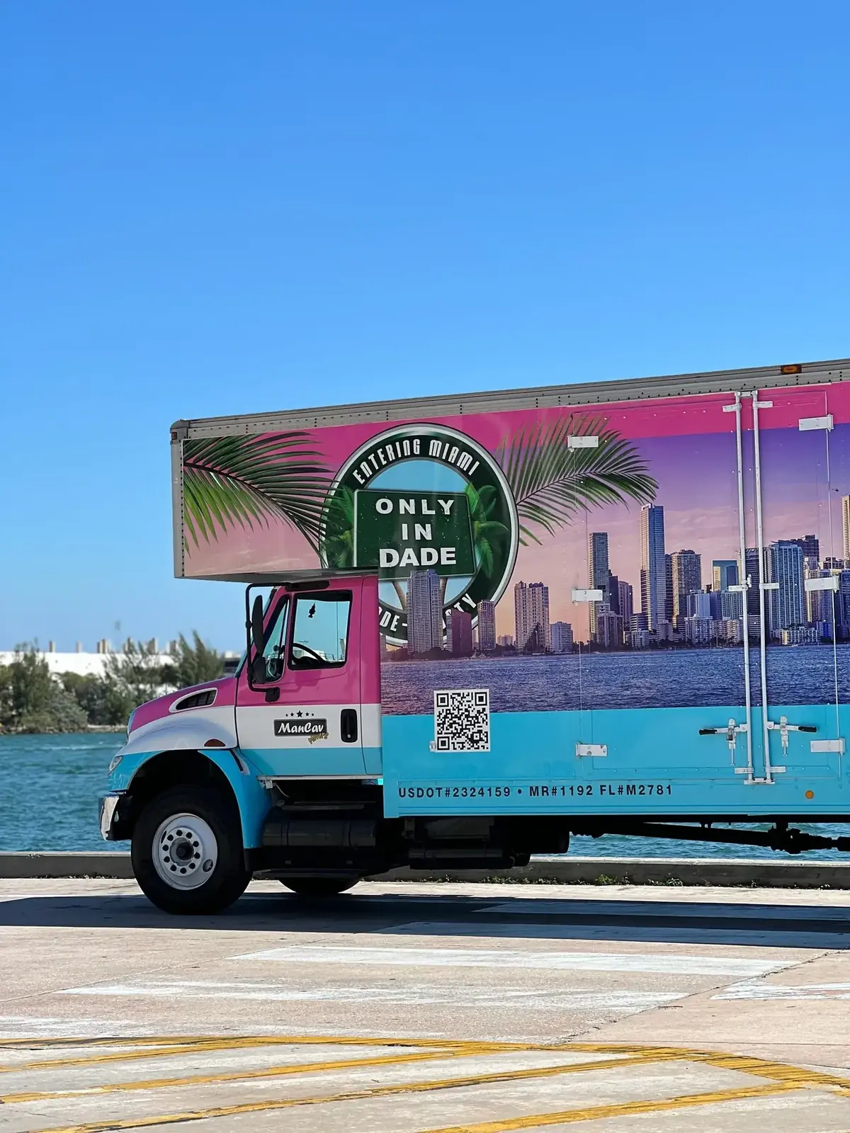 ManCav Movers truck with Miami skyline wrap on the waterfront; USDOT and FL mover numbers visible